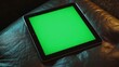 © Aisha - A tablet with a green screen resting on a smooth, leather surface with reflections of ambient light