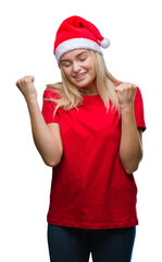 Wall Mural - Young caucasian woman wearing christmas hat over isolated background very happy and excited doing winner gesture with arms raised, smiling and screaming for success. Celebration concept.