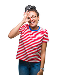 Wall Mural - Young braided hair african american girl wearing glasses over isolated background doing ok gesture with hand smiling, eye looking through fingers with happy face.