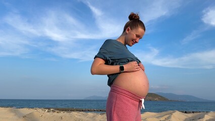 Wall Mural - Happy young pregnant woman relax on the beach, sea, enjoying summer vacation, touching her big belly