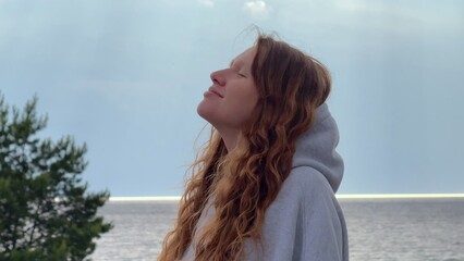 Wall Mural - Young woman enjoying weather on sea, beach, breath deep fresh air, raise her arms at rain