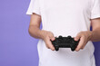© New Africa - Man playing video games with controller on violet background, closeup. Space for text