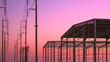 © Prapat - Silhouette of 2 industrial building framework structure in factory construction site with electric poles and cable lines against orange pink twilight sky background, perspective side view