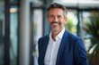 © Deris Firmansyah - Headshot close up portrait of indian or latin confident mature good looking middle age leader, ceo male businessman in suit on office background. Handsome hispanic senior business man smile at camera