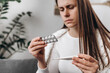 © Yura Yarema - Close up of sick young woman have fever, cough and sore throat, holding thermometer for check measure body temperature, girl hold pill medicine pack reading label text about medical information