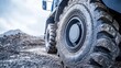 © VirtualVista - Close up of large construction truck tire showcasing worn rubber and intricate tread patterns on rough terrain in an industrial setting