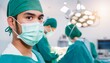 © photostockatinat - Focused Surgeon in Operating Room: A determined surgeon, wearing a surgical mask and cap, stares intently at the camera.