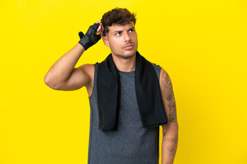 Wall Mural - Young sport caucasian man with towel isolated on yellow background having doubts and with confuse face expression