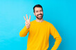 © luismolinero - Young caucasian man over isolated blue background happy and counting three with fingers