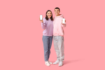 Young couple showing mobile phones on pink background. Online dating