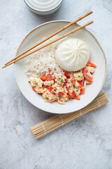 Wall Mural - Tomato egg-stir fry with steamed rice and baozi, flat lay on a white stone background, vertical shot with space