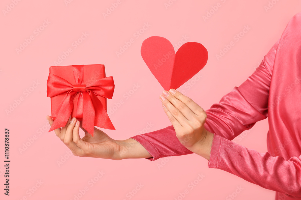 Female hands with gift box and paper heart on pink background. Valentine's Day celebration