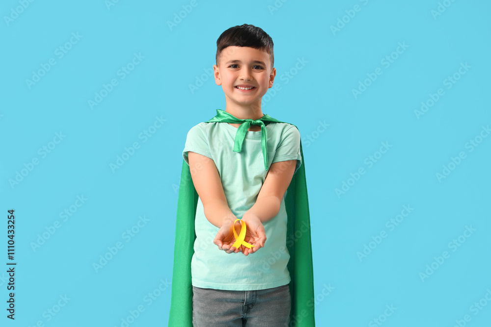 Little boy dressed as superhero with gold ribbon on blue background. Childhood cancer awareness concept