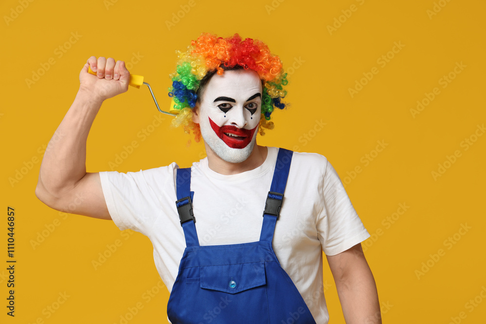 Young man as clown in jumpsuit with roller on yellow background