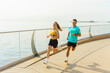 © muse studio - Energetic couple jogging along a scenic waterfront promenade on a sunny day
