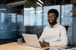 © Liubomir - African American man businessman typing on laptop in modern office setting. Wearing glasses, white shirt, looking confident and professional. Ambient reflects on glass walls, creating a sleek vibe.