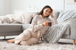 © Pixel-Shot - Beautiful young woman with glass cup of hot cocoa sitting on carpet in living room