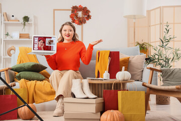 Wall Mural - Beautiful young woman with autumn clothes and laptop sitting on sofa at home. Online shopping concept