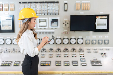 Wall Mural - Asian female engineer supervisor looks at the system with laptop and in the machine room of a large industrial wind and steam power plant, wearing a hard hat and uniform.