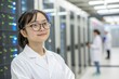 © SerPak - A young woman wearing glasses and a lab coat stands with her arms crossed in a data center. Rows of servers illuminate the background, showcasing a high tech environment during work hours.