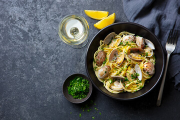 Wall Mural - Spaghetti alle vongole, seafood pasta with clams in a black bowl and glass of wine. Dark background. Copy space. Top view.