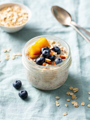 Wall Mural - Overnight oats with fresh berries and fruits in glass jars. Blue textile background. Close up.