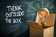 © Ignats - Creative concept of innovation featuring a glowing light bulb emerging from a cardboard box against a chalkboard background with the phrase “Think Outside the Box”