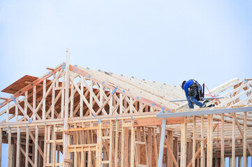 Wall Mural - A construction worker atop a two-story wooden home under construction in a new housing development uses a power tool