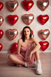 © Adam - Woman in a pink ruffled dress and white boots sitting on the floor with heart-shaped balloons in the background