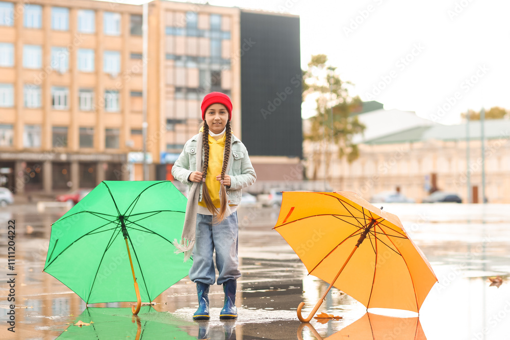 Cute little girl with umbrellas jumping in puddle on rainy day outdoors ...
