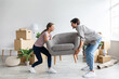 © Prostock-studio - Smiling caucasian millennial wife and husband carry armchair in room with cardboard boxes. Moving together to new house, buy furniture. Purchases apartment on mortgage and loan, rent real estate