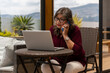 © FABIAN PONCE GARCIA - Elderly woman talks on her cell phone while looking at her laptop on a terrace
