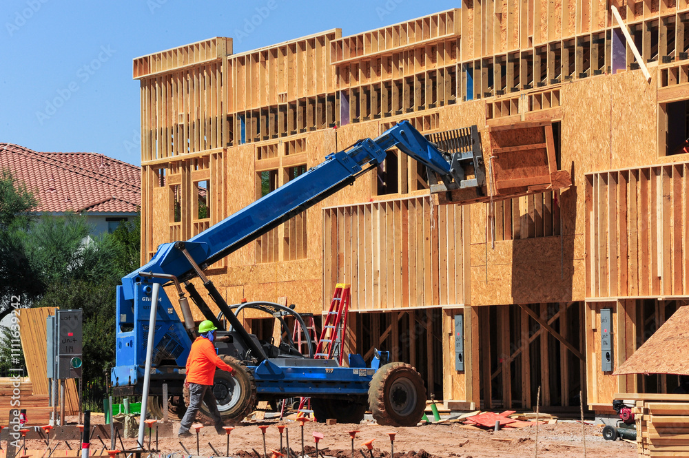 A construction worker wearing a hard hat walks past a telehandler ...