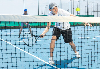 Wall Mural - Young man in shorts and t-shirt playing tennis on court. Racket sport training outdoors