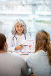 © Kittipong - A professional senior Asian female doctor in a uniform having a consultation with a young married couple in the examination room. doctor visit, health care, medical