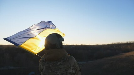 Wall Mural - Female ukrainian army soldier lifting national banner in hill. Young woman in military uniform waving flag of Ukraine against background of sunset. Victory at war. Resistance to russian invasion