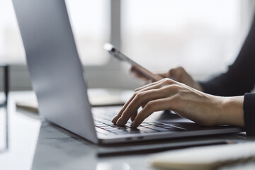 Wall Mural - With a softly blurred office scene in the background, the image reveals a close-up of a woman's hands typing on a stylish laptop keyboard