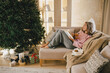 © polinaloves - Young woman relaxing, reading book and drinking cocoa in a cozy living room near Christmas tree.