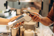 © Maria Vitkovska - Customer is holding his smartphone over a payment terminal, making a contactless payment for his coffee at the counter of a coffee shop