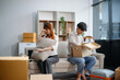 © laddawan - Young couple preparing for a move, packing boxes and a suitcase in a cozy living room.