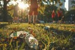 © Tixel - A park scene where empty plastic bottles and autumn leaves cover the grassy ground, with people enjoying the recreational area in the background, highlighting pollution.