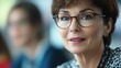 © Morning - A woman wearing glasses looks thoughtfully to the side in a meeting setting.