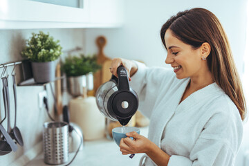 Wall Mural - Smiling Woman in White Robe Making Morning Coffee in Modern Kitchen