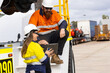 © Austockphoto - Two workers wearing high visibility clothing man sitting on the truck while woman showing the tablet