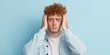 © kiimoshi - A young man experiencing stress or frustration, holding his head against a blue backdrop.