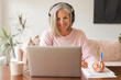 © Tatyana Gladskih - Happy middle aged online course student in headphones learning watching webinar on laptop