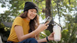 © ChayTee - Gen Z eco go green woman asia sit happy relax at tree public park city life enjoy typing mobile phone drink coffee bottle use reuse tote bag care save the earth planet net zero waste clean future hope