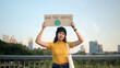 © ChayTee - Go green Gen Z woman asia young people looking at camera stress showing save the earth planet world care banner poster sign in city nature tree. Protect global warming future asian hope net zero waste