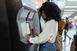 © bernardbodo - Young black woman buying train ticket at self-service kiosk in subway station