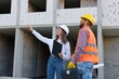 © nazariykarkhut - Female architect pointing at something while discussing with construction worker at building site